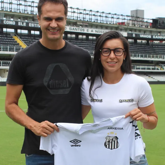 Thiago Taveira ao lado de uma atleta no gramado de um estádio